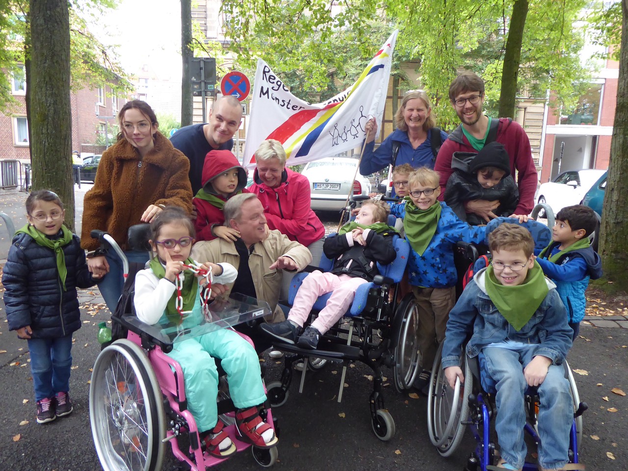 Schauspieler Axel Prahl hockt lächelnd inmitten einer Gruppe von Schüler*innen der Regenbogenschule