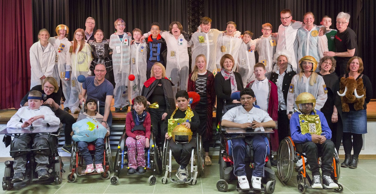 Die Schauspielerinnen und Schauspieler des Theaterstücks stehen gemeinsam in ihren Kostümen auf der Bühne für ein Gruppenbild.