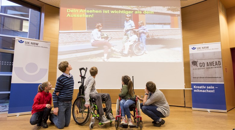 Die Schüler_innen und Lehrerin der M3b folgen auf der Bühne der Präsentation ihres Videos.