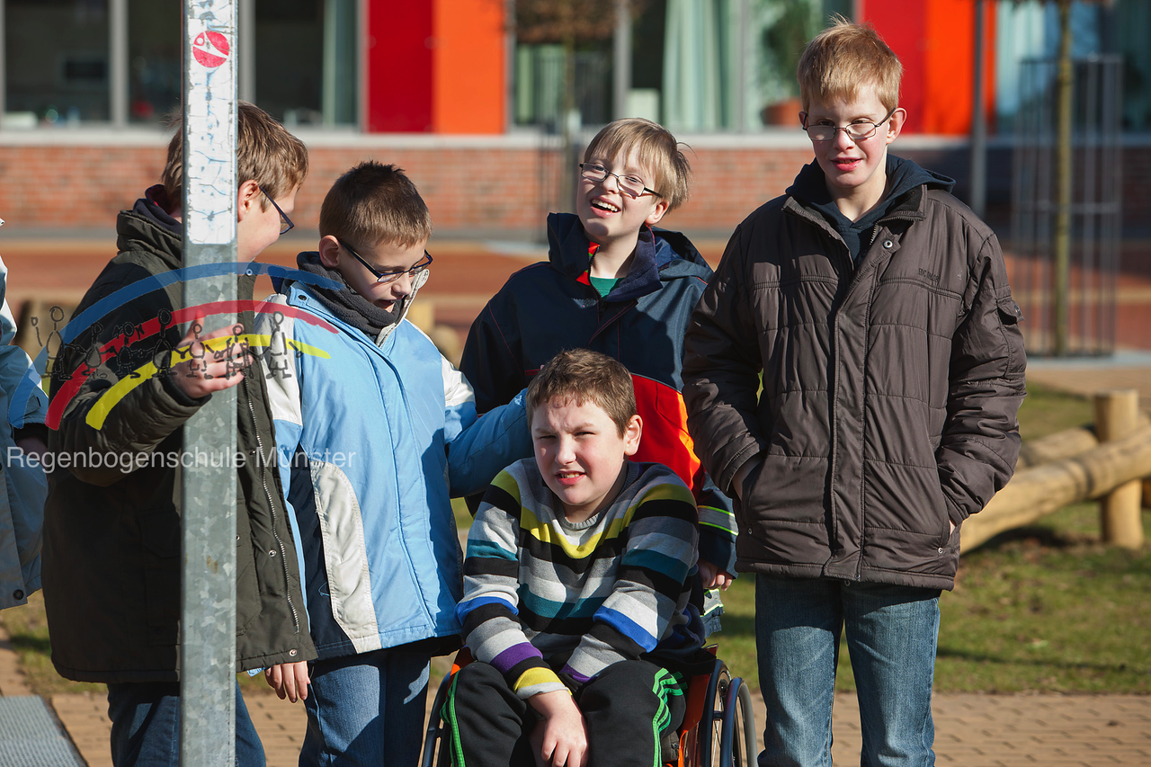 Bild der Kategorie "Schulleben". Fünf Schüler stehen und sitzen zusammen auf dem Schulhof und lächeln in die Kamera.